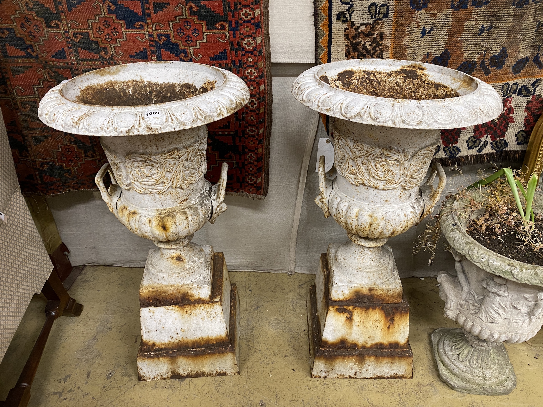 A pair of painted cast iron campana garden urns on stepped square plinths, diameter 46cm, height 90cm